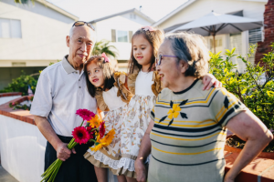 An older man and an older woman stand on either side of two young girls, and the girls have their arms around the older individuals